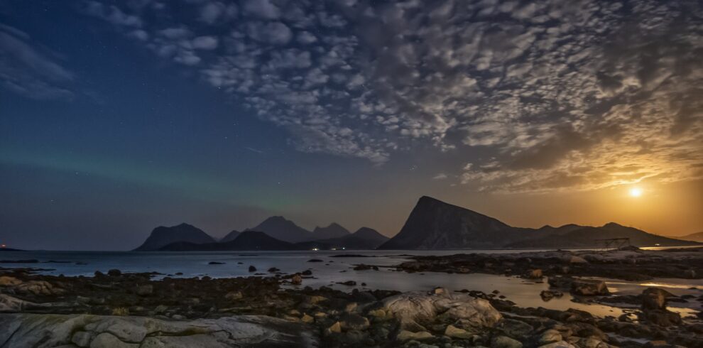 Magnificent landscape of sea waving on rocky coast near mountains in Lofoten archipelago against sunset sky